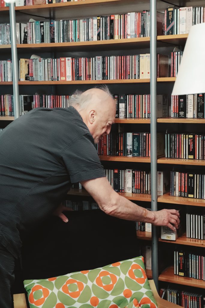 Auf dem Bild ist Josef von der Seite zu sehen. er bückt sich herunter um eine CD aus dem vollbepackten Regal zu holen