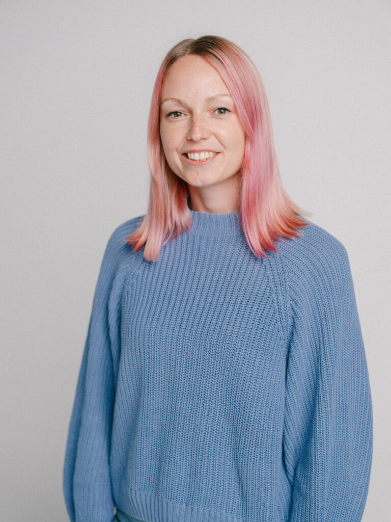 Eine junge Frau mit rosa Haaren schaut in die Kamera.