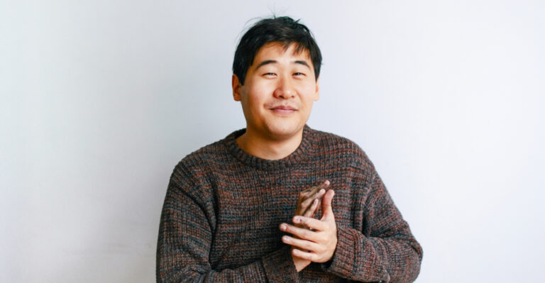 Auf diesem Foto sieht man den Künstler Juewen Zhang. Er sieht mit freundlichem Blick in die Kamera. Er trägt einen braunen Pullover.