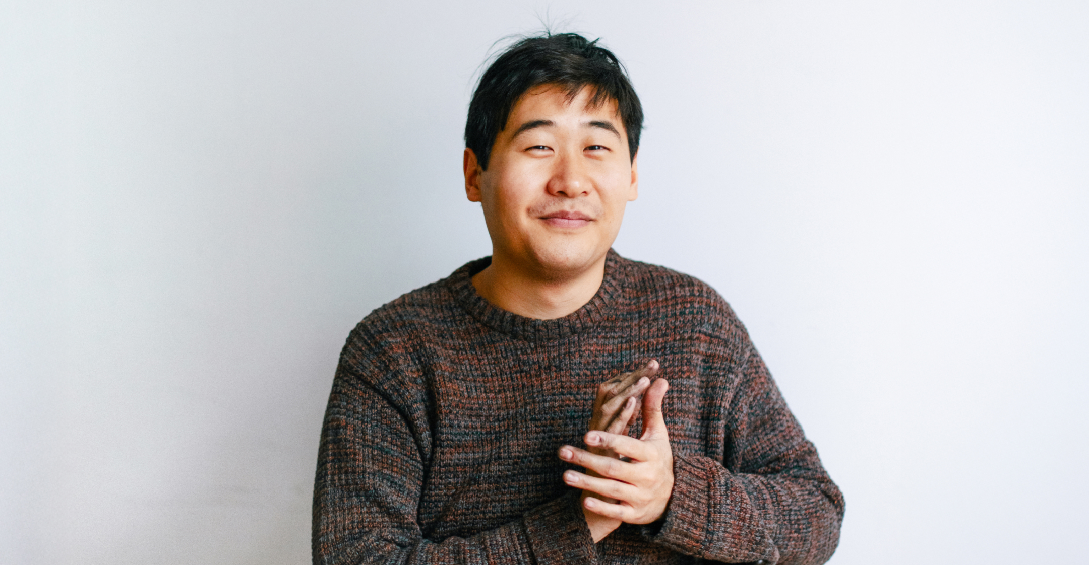 Auf diesem Foto sieht man den Künstler Juewen Zhang. Er sieht mit freundlichem Blick in die Kamera. Er trägt einen braunen Pullover.