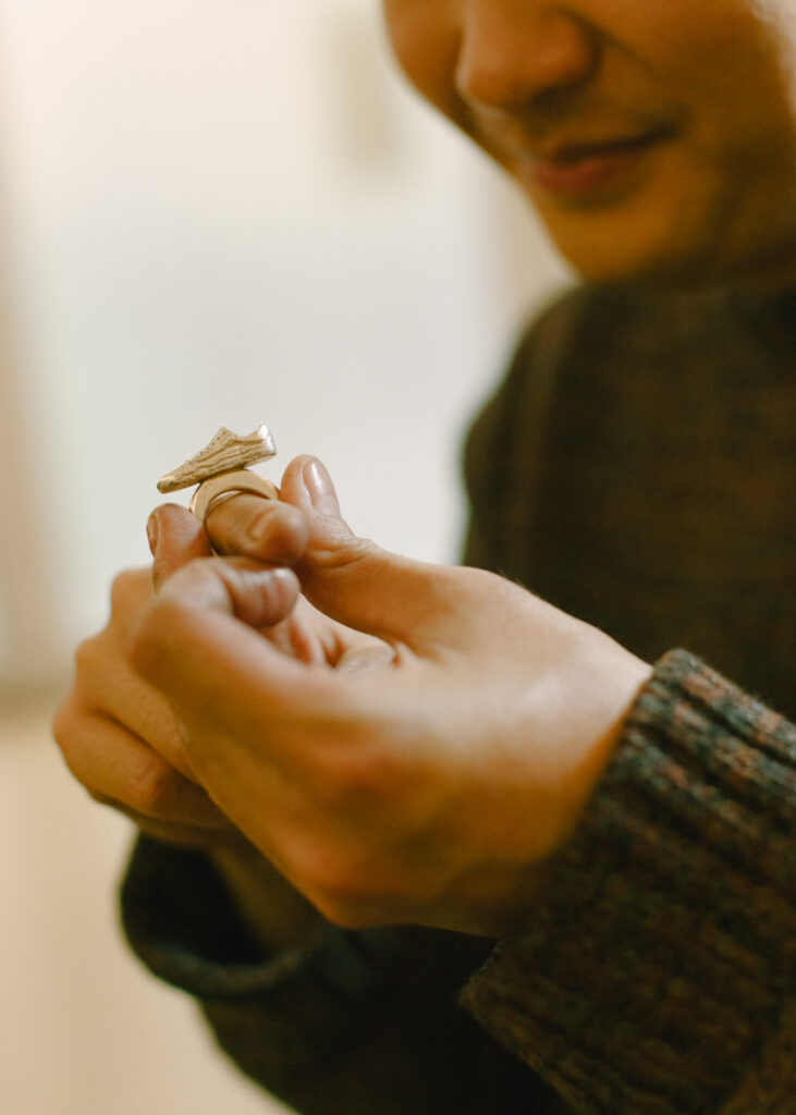 Juewen Zhang hält einen kleinen Ring in der Hand. Auf dem Ring ist eine Miniatur eines Van-Schuhs. Er betrachtet ihn mit einem Lächeln.