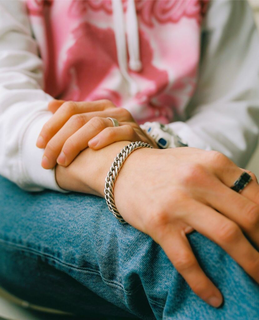 Das Foto zeigt zwei Hände, die übereinander liegen. Die Person trögt auf jeder Hand einen Ring und auf der rechten Armgelenk ein Armband.